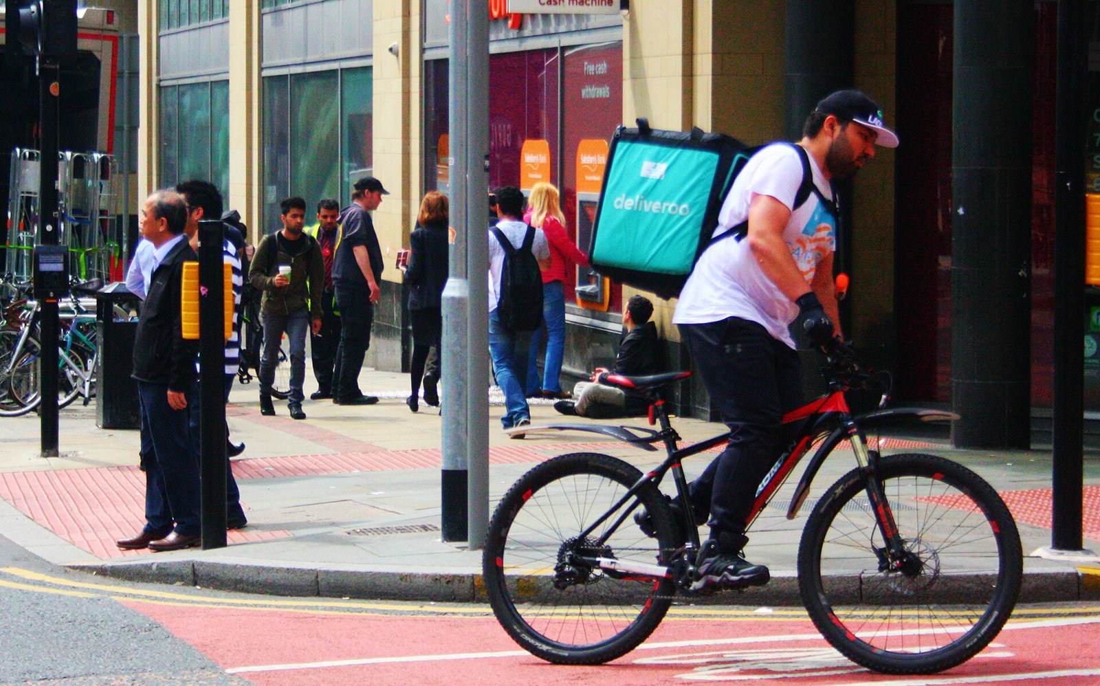A food delivery courier with an insulated backpack rides a bike through a busy city street.