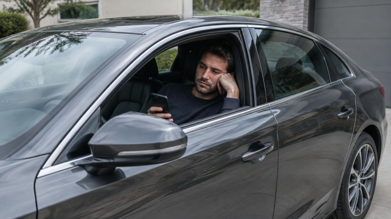 Man looking bored inside a shiny new car in his driveway
