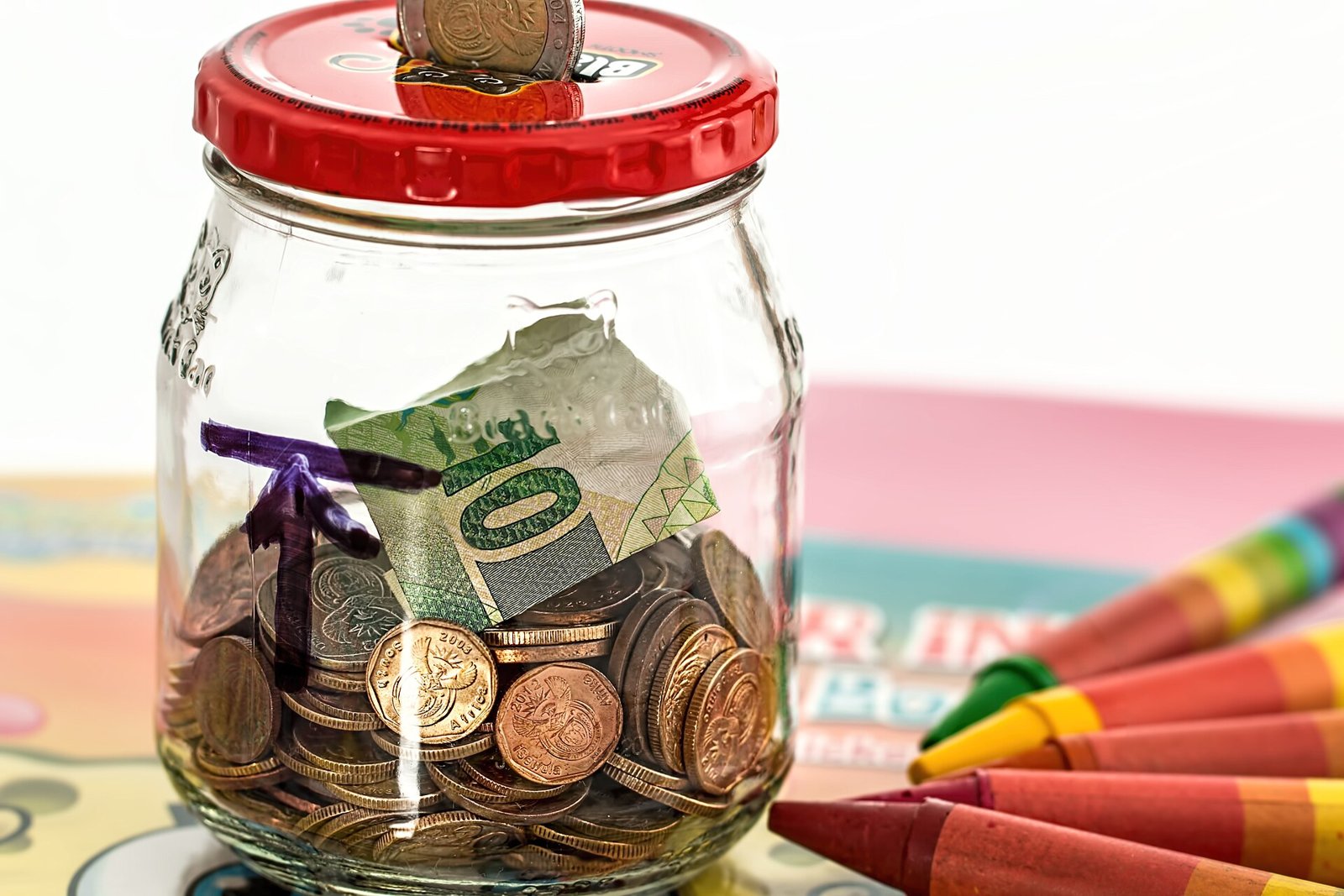 A glass savings jar filled with coins and folded cash.