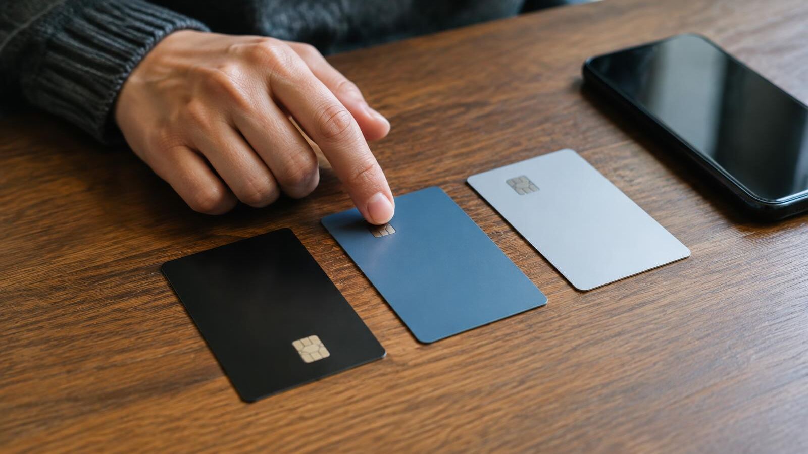 Hand choosing between three credit cards on a table