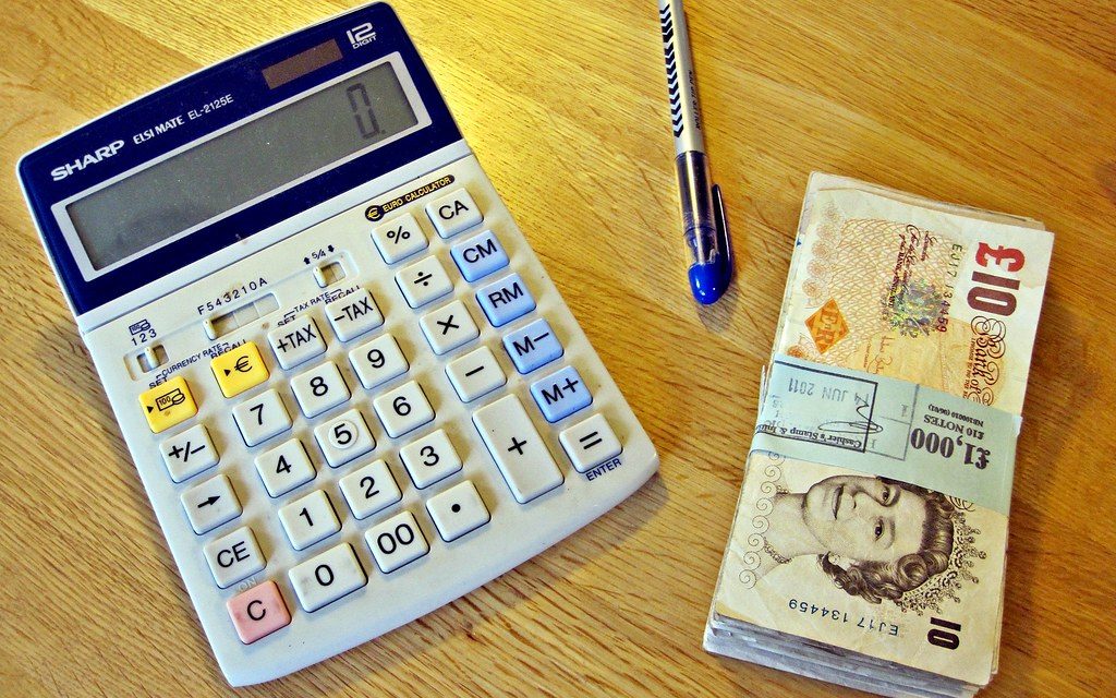 A calculator, pen and banknotes on a desk