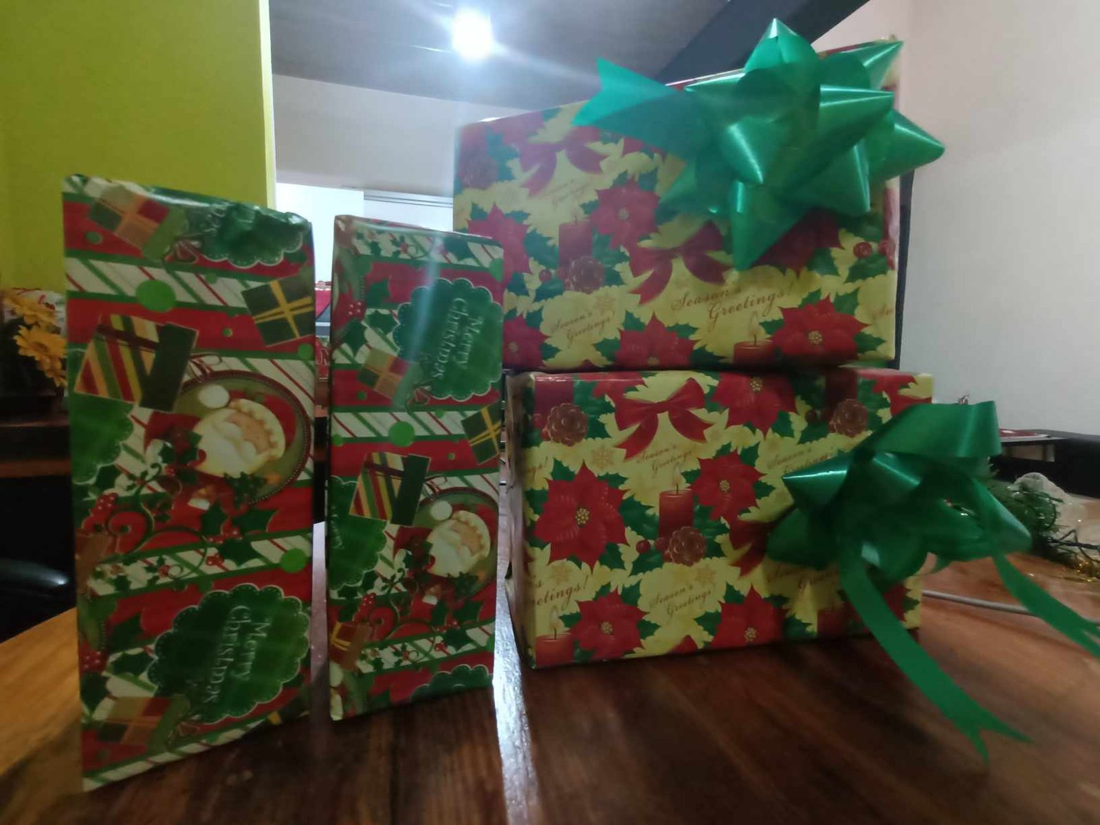 Holiday gifts wrapped in festive paper with green bows on a table.