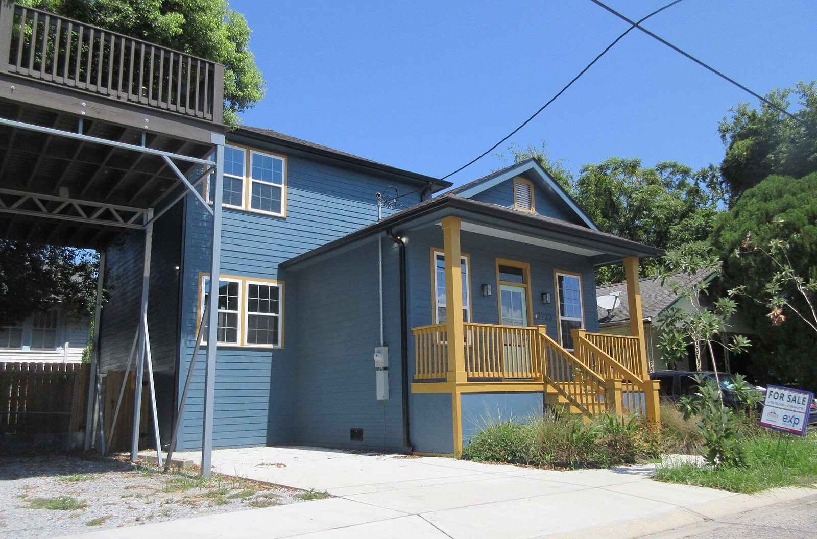 A newly built blue house with a for-sale sign on a quiet street.