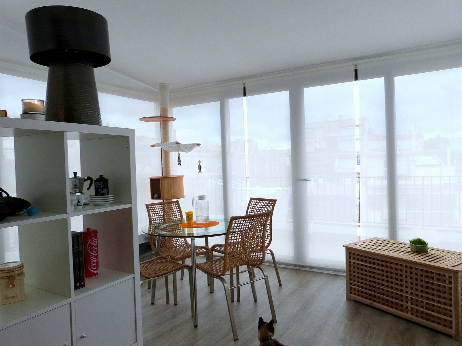 A bright apartment living area with shelves, a small table and large windows.