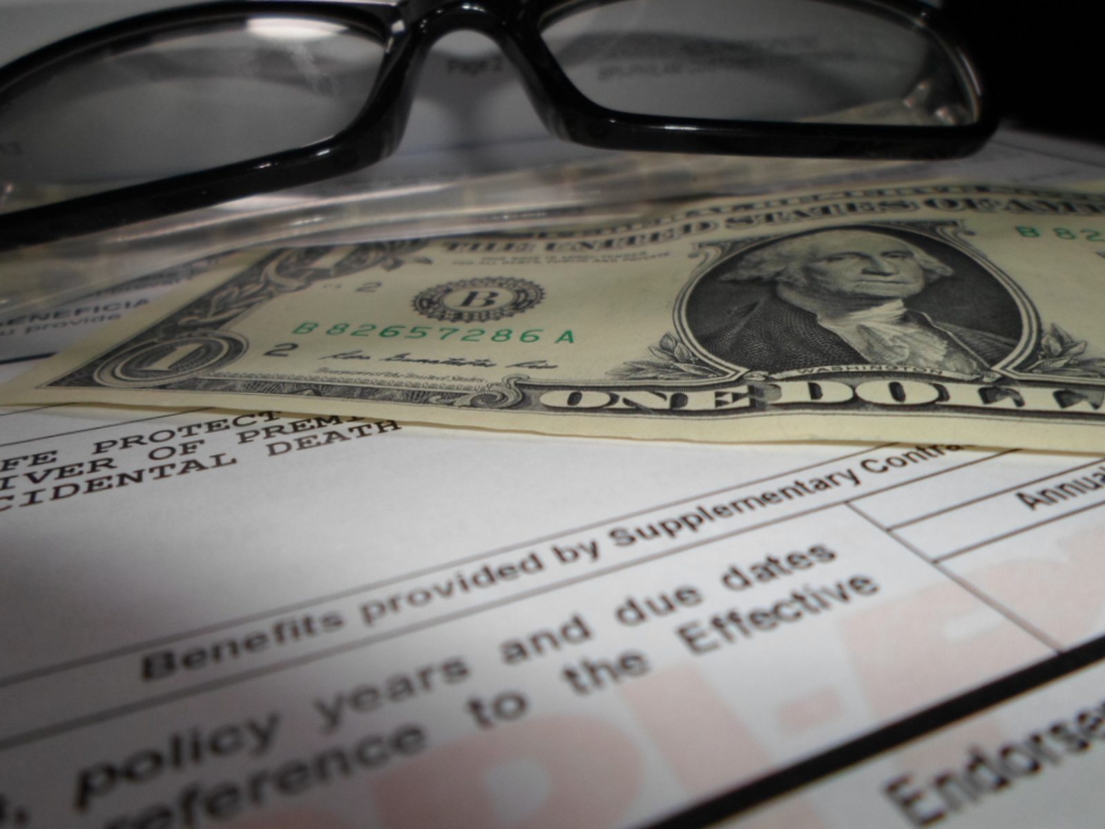 A life insurance policy document with a dollar bill and reading glasses resting on it.