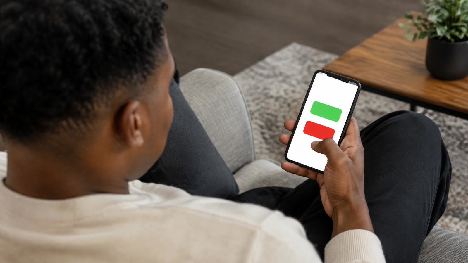 A man on his couch choosing between a green and a red button on his phone