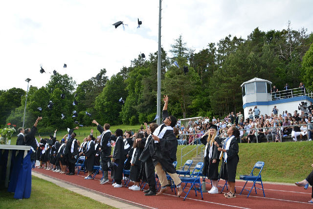 Graduates toss their caps into the air at an outdoor commencement ceremony.