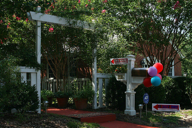 An Open House sign and a For Sale by Owner sign outside a brick house with a white garden arbor