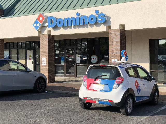 A Domino's Pizza store with the Domino's sign and a branded delivery car parked out front