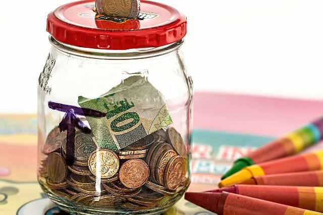 A glass jar used as a homemade savings jar, holding coins and a folded banknote