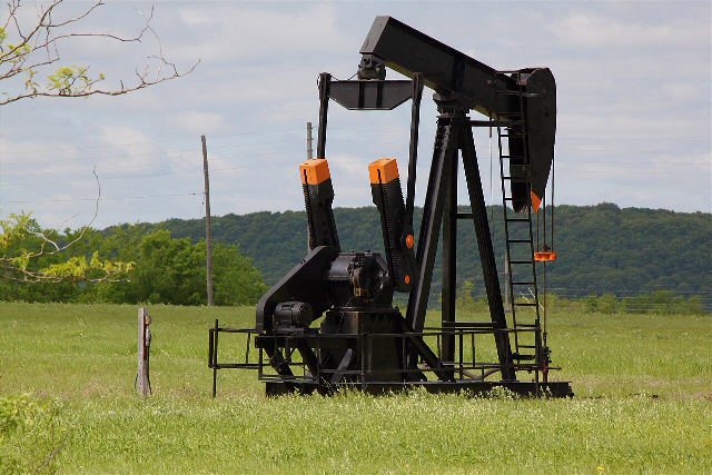An oil pumpjack in a green field at the Glenn Pool oil field in Oklahoma
