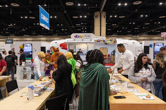 An eBay Live booth with the eBay Live sign above a streaming trailer at MegaCon 2026 in Orlando, Florida, with shoppers looking at trading cards
