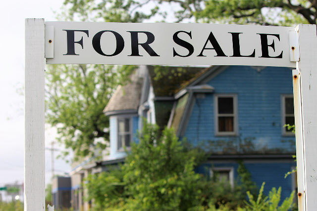 A white For Sale sign in front of a blue two-story house in Niskayuna, New York