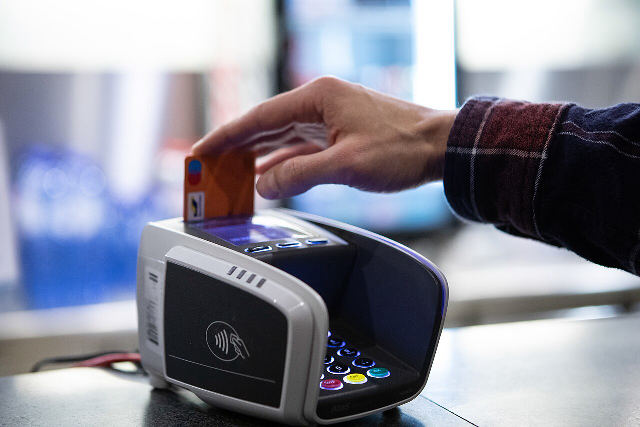 A hand tapping a bank card on a contactless card payment terminal at a shop counter